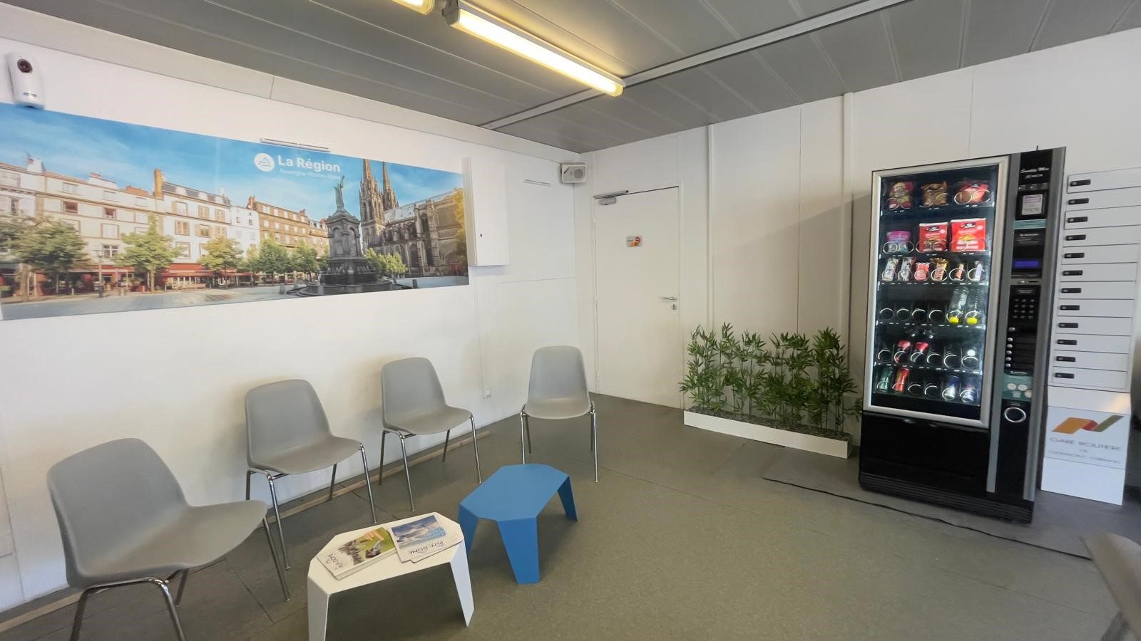 Salle d'attente de la gare : sièges, distributeur de boissons et confiseries, espace lumineux.